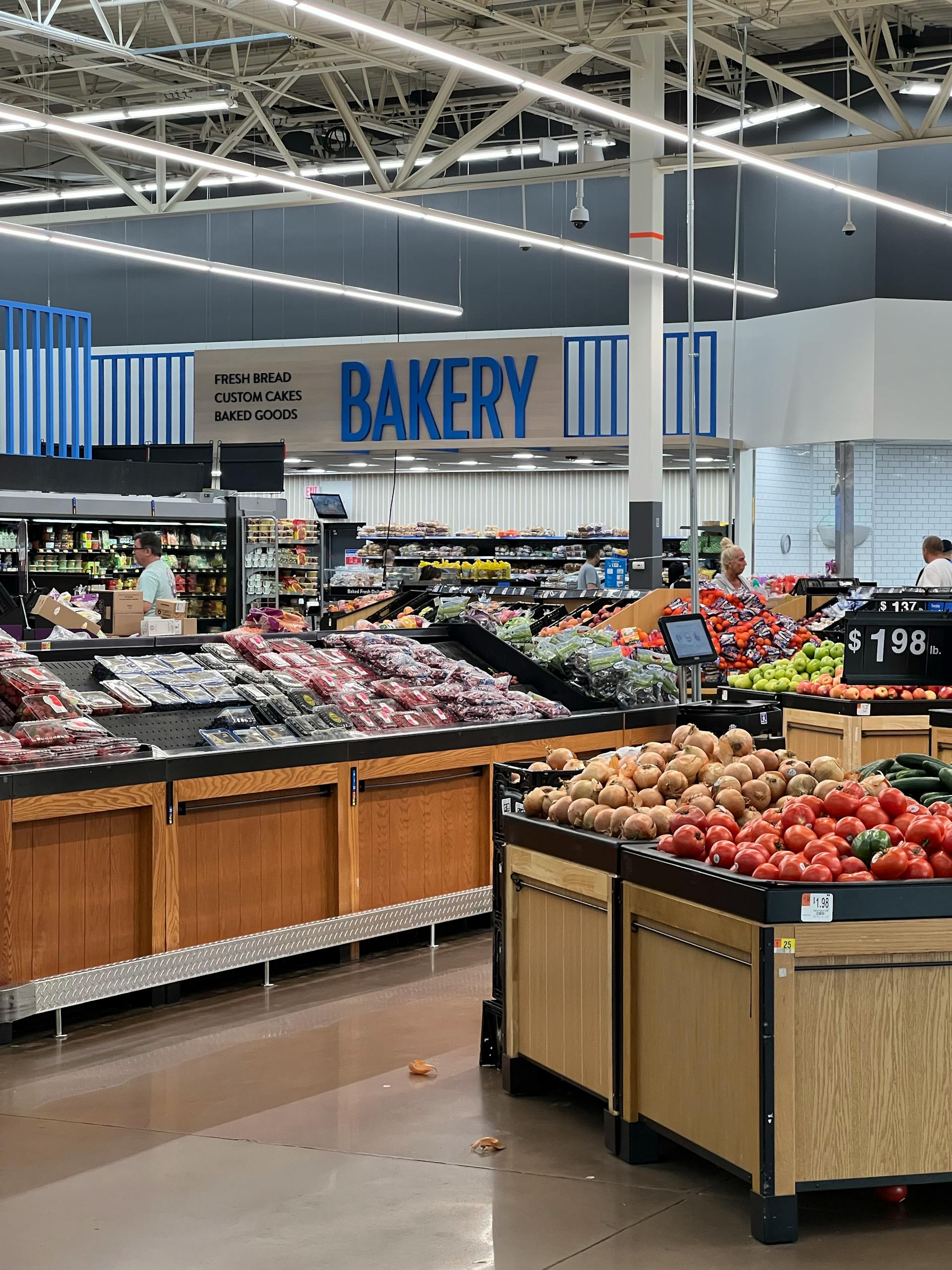 Modern grocery store produce section with fresh fruits and bakery signs.